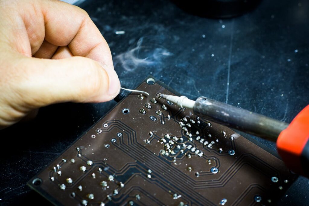 Hand soldering on a printed circuit board, showcasing electronic craftsmanship.